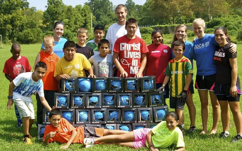 Kids and leaders from the Southwood soccer camp posing behind a stack of new soccer balls on the field