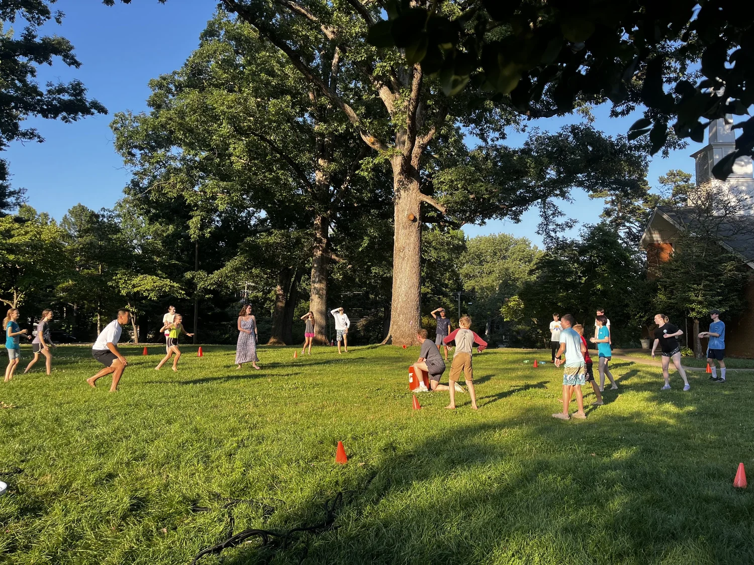 Youth playing a field game on the churchyard lawn beside the steeple on a summer evening