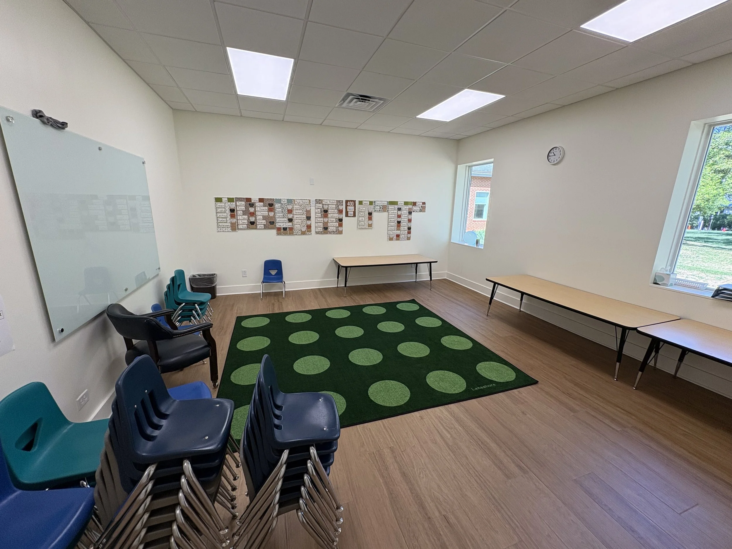 A new children's classroom with a green play rug, tables, and stacked chairs
